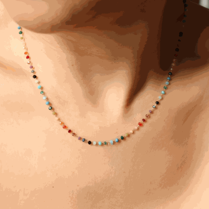 Close-up of a delicate rainbow gemstone beaded necklace with multicolored small crystals on a gold chain
